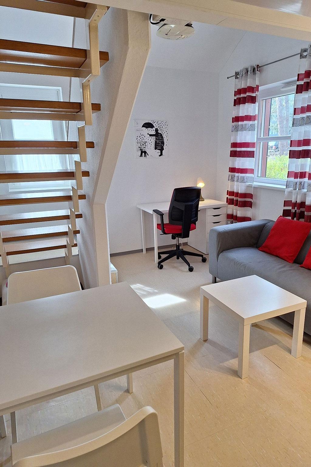 View of a room with table, desk, couch and stairs.