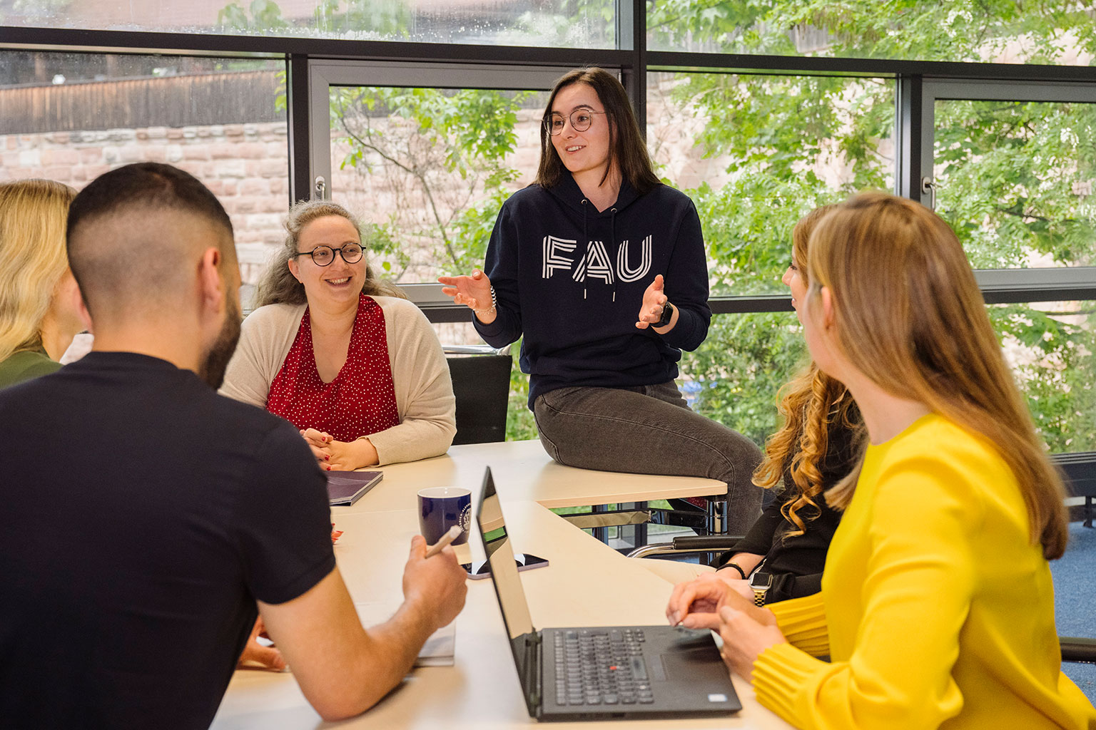 Mehrere Frauen und Männer sitzen gemeinsam an einem Tisch und disktuieren miteinander.