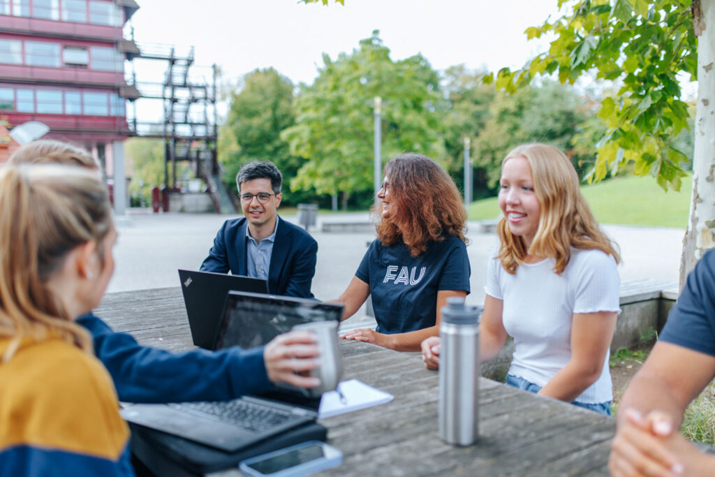 Mehrere Personen sitzen mit Laptops an einem Tisch im Freien.