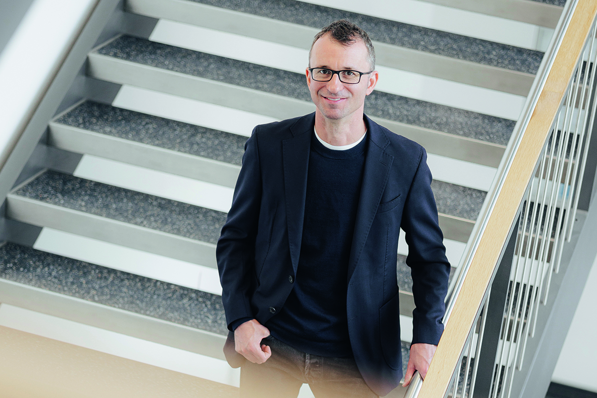 Dr. Wieland, ein Mann mit Brille, geheimratsecken und im schwarzen Jacket, lächelt aus der Vogelperspektive in die Kamera.
